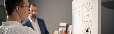 LBS-Berater steht an Whiteboard und wird von LBS-Gebietsleiter gecoacht. 